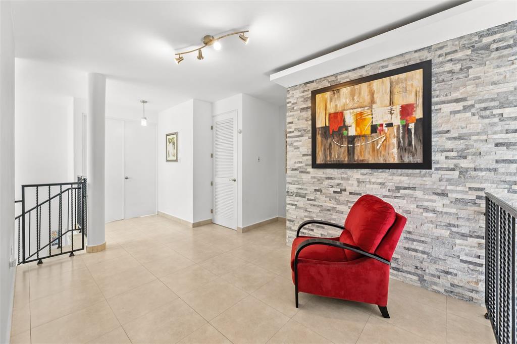 A bright hallway features a red armchair, a stone accent wall, and tiled flooring — JASPER ST. TREASURE POINT UNIT 50, VEGA ALTA, PR