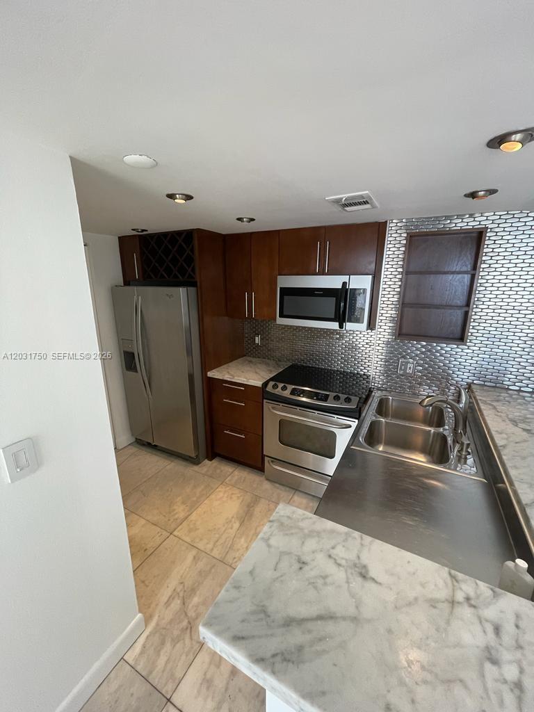 A kitchen features dark wood cabinets, stainless steel appliances, and a marble-patterned countertop — 770 Claughton Island Dr # 1504, Miami FL 33131, MIAMI, FL
