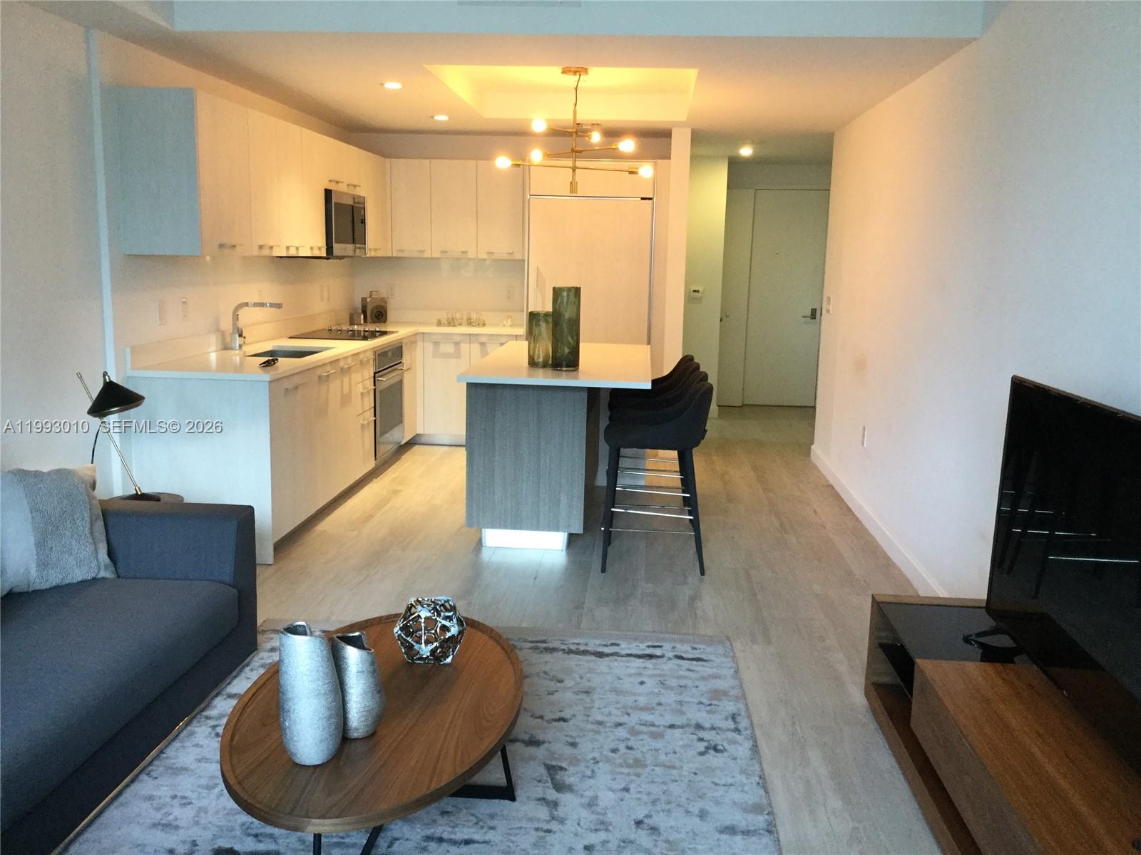 An open-concept kitchen and living area features white cabinetry, a central island, and wood flooring — 55 SW 9th St # 1905, Miami FL 33130, MIAMI, FL