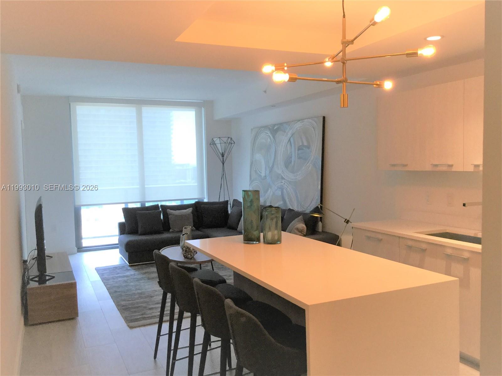 A modern open-concept living area features a kitchen island, dining stools, and a gray sofa — 55 SW 9th St # 1905, Miami FL 33130, MIAMI, FL