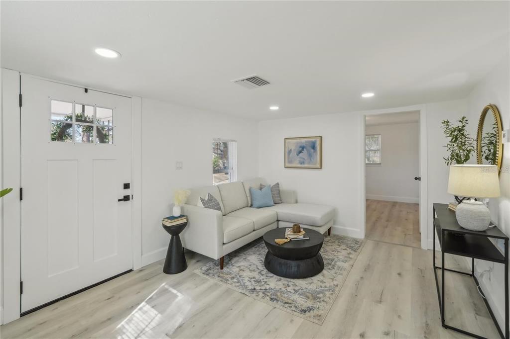 A bright living room features white walls, light wood flooring, a sectional sofa, and entryway — 2111 E ELLICOTT STREET, TAMPA, FL