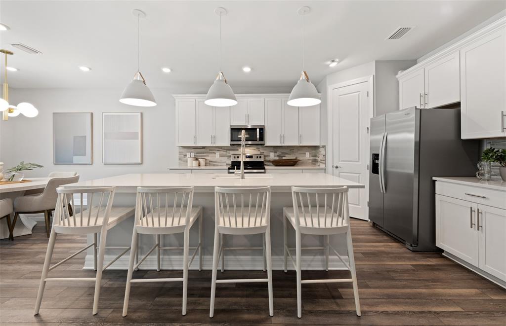 A modern kitchen features white cabinetry, a large island with four stools, and stainless appliances — 7437 SUMMER COURT, SARASOTA, FL