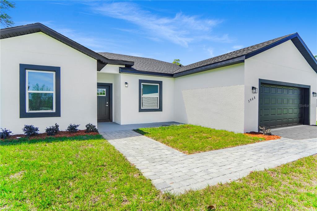 A single-story house with white stucco walls, dark trim, and a paved walkway — 3908 SW 171ST LANE, OCALA, FL