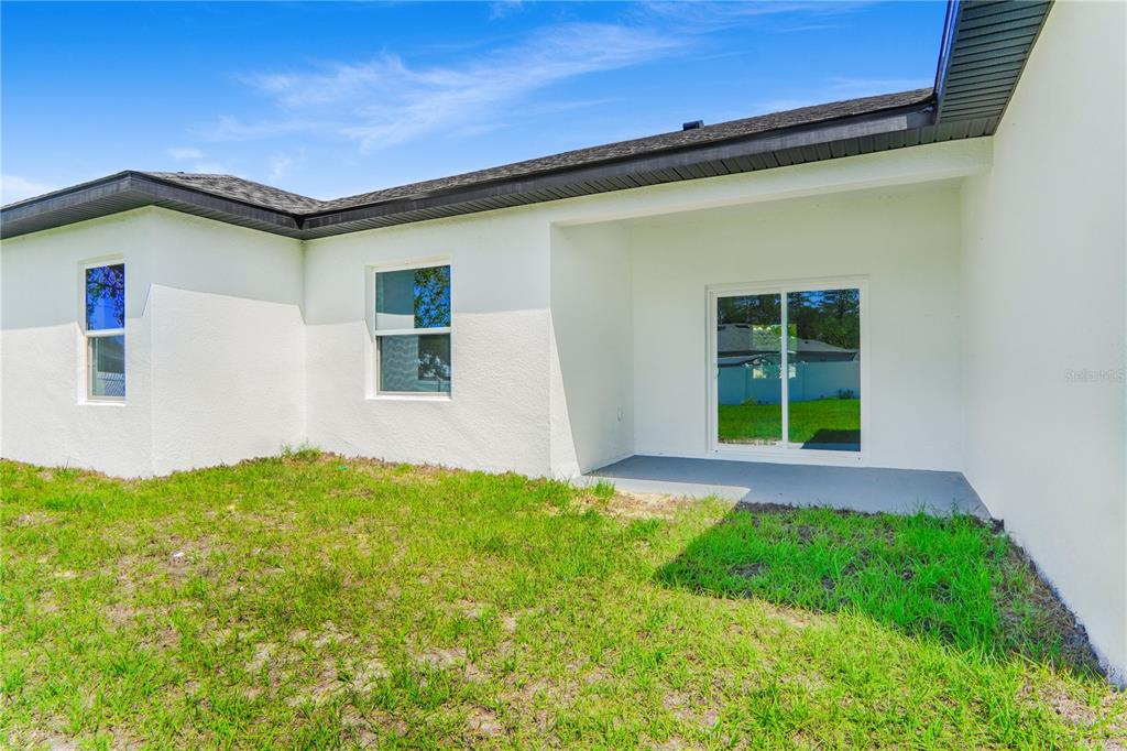 A white stucco house exterior features a covered patio with a sliding glass door — 3908 SW 171ST LANE, OCALA, FL