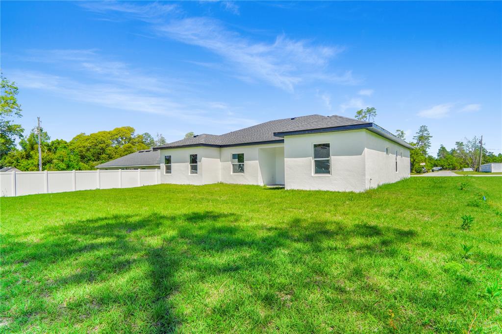 The rear exterior of a white, single-story house with a lawn and vinyl fence — 3908 SW 171ST LANE, OCALA, FL