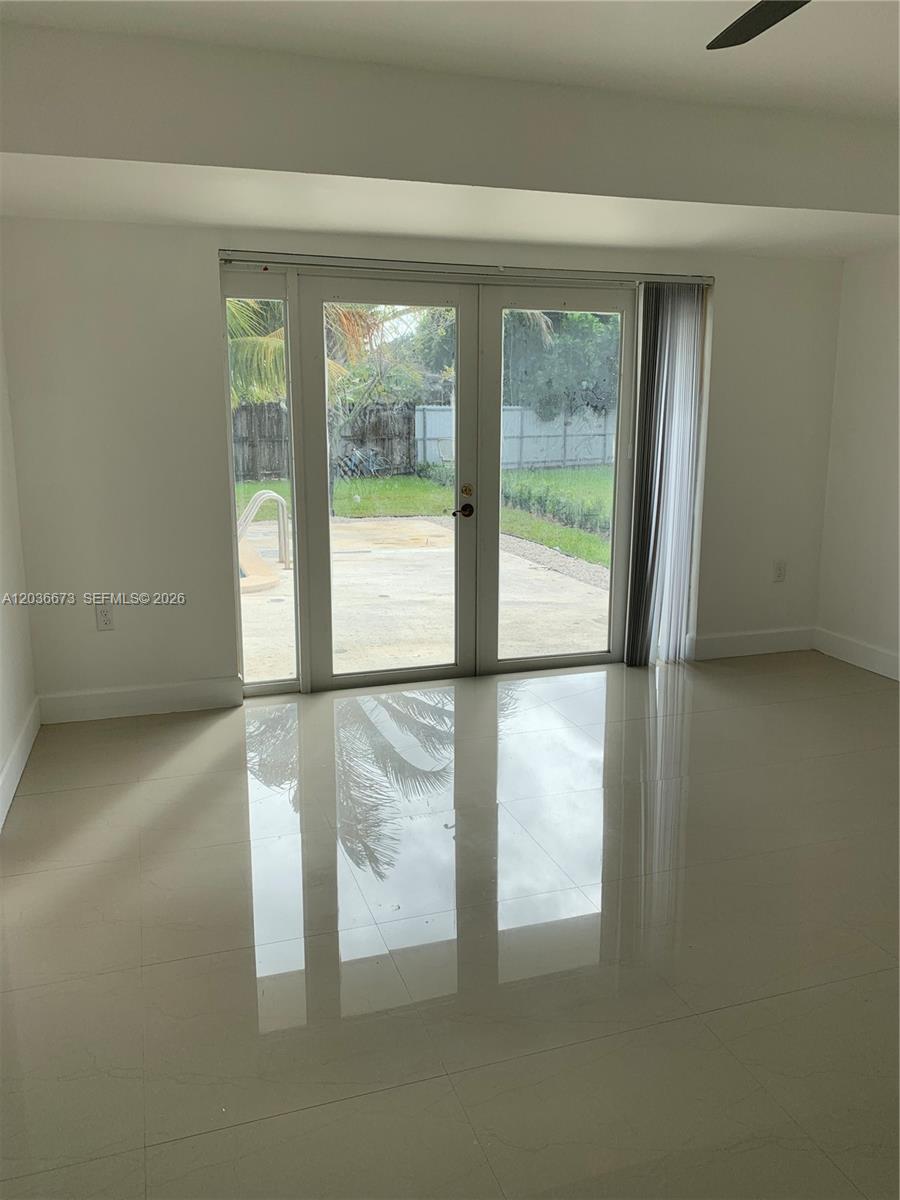 A room with light-colored tile flooring features double glass doors opening to a backyard patio — 2025 SW 84th Ct, Miami FL 33155, MIAMI, FL