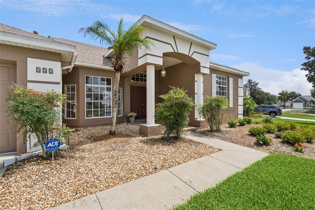 The exterior of a tan stucco house features a covered entryway, palm tree, and landscaping — 232 VIA MARIEL EAST DRIVE, DAVENPORT, FL