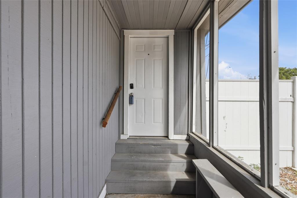A white front door is accessed by three gray steps inside a screened-in porch — 920 E ANNIE STREET, TAMPA, FL