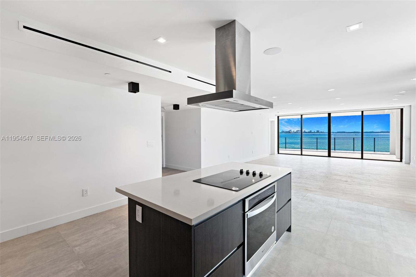 A modern kitchen island with a cooktop and oven faces a living area with water views — 1930 Bay Dr Second Level Un # 1, Miami Beach FL 33141, MIAMI BEACH, FL