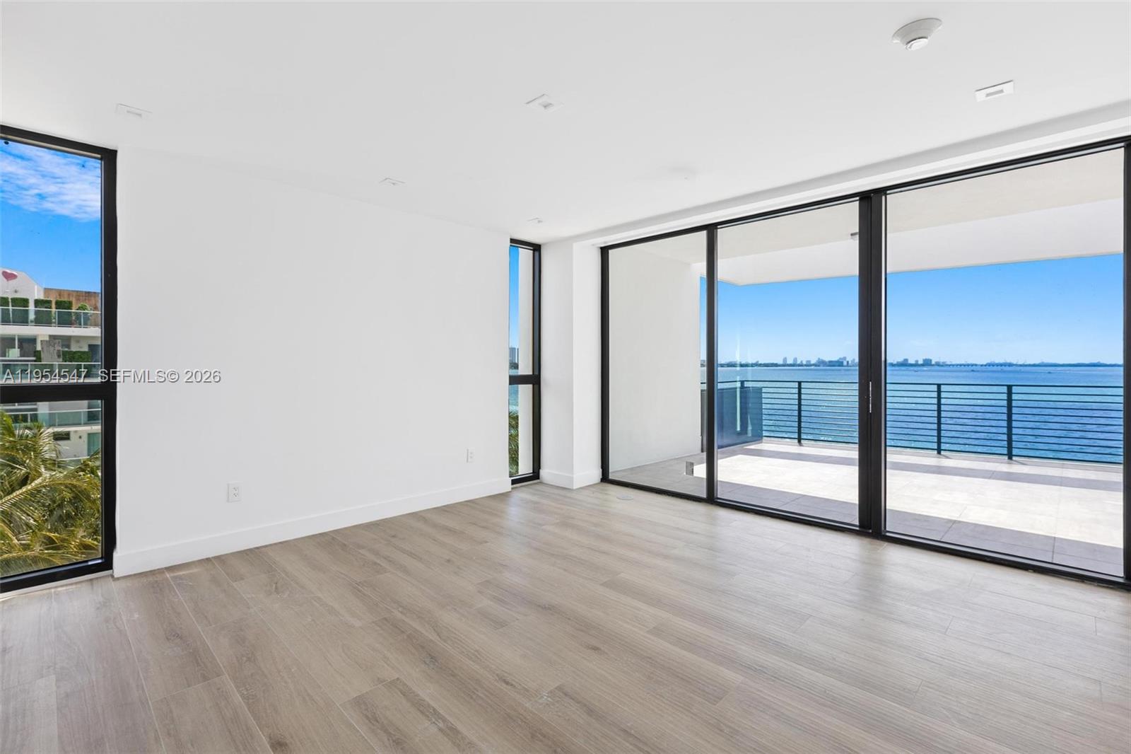 An empty room features light wood-look flooring, white walls, and large sliding glass doors — 1930 Bay Dr Second Level Un # 1, Miami Beach FL 33141, MIAMI BEACH, FL
