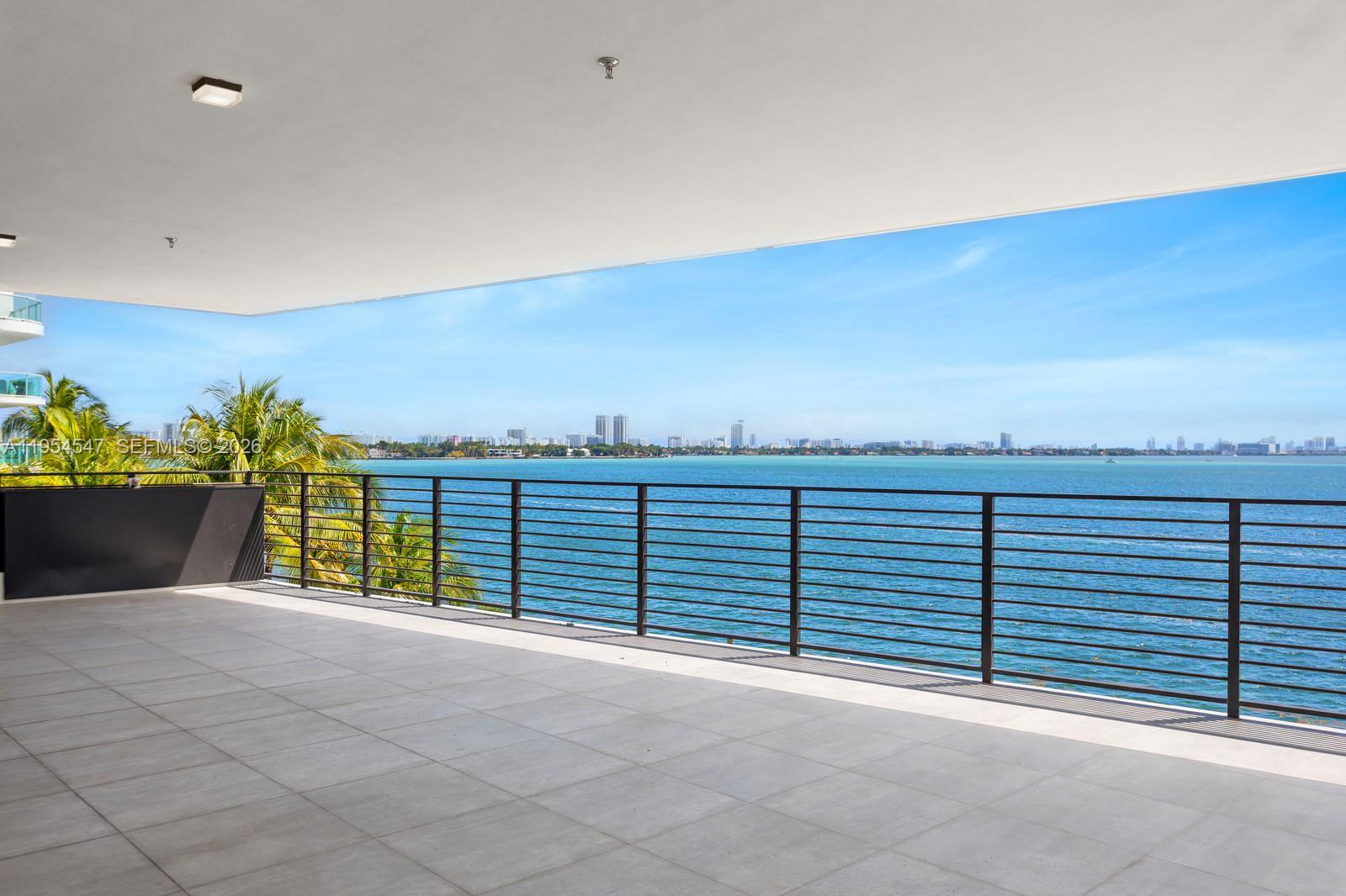 A spacious balcony with light gray tile flooring overlooks the ocean and a distant city — 1930 Bay Dr Second Level Un # 1, Miami Beach FL 33141, MIAMI BEACH, FL