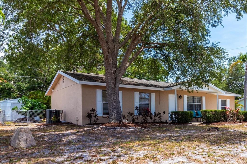A single-story tan house with white shutters sits behind a large tree in a yard — 3314 ISLAND DATE CIRCLE, SARASOTA, FL