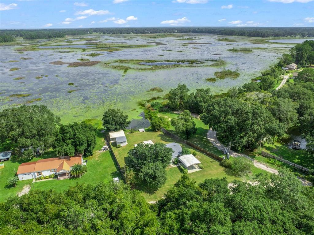 An aerial view shows two houses on a grassy lot bordering a large, marshy lake — 11495 SE 121ST LANE ROAD, BELLEVIEW, FL