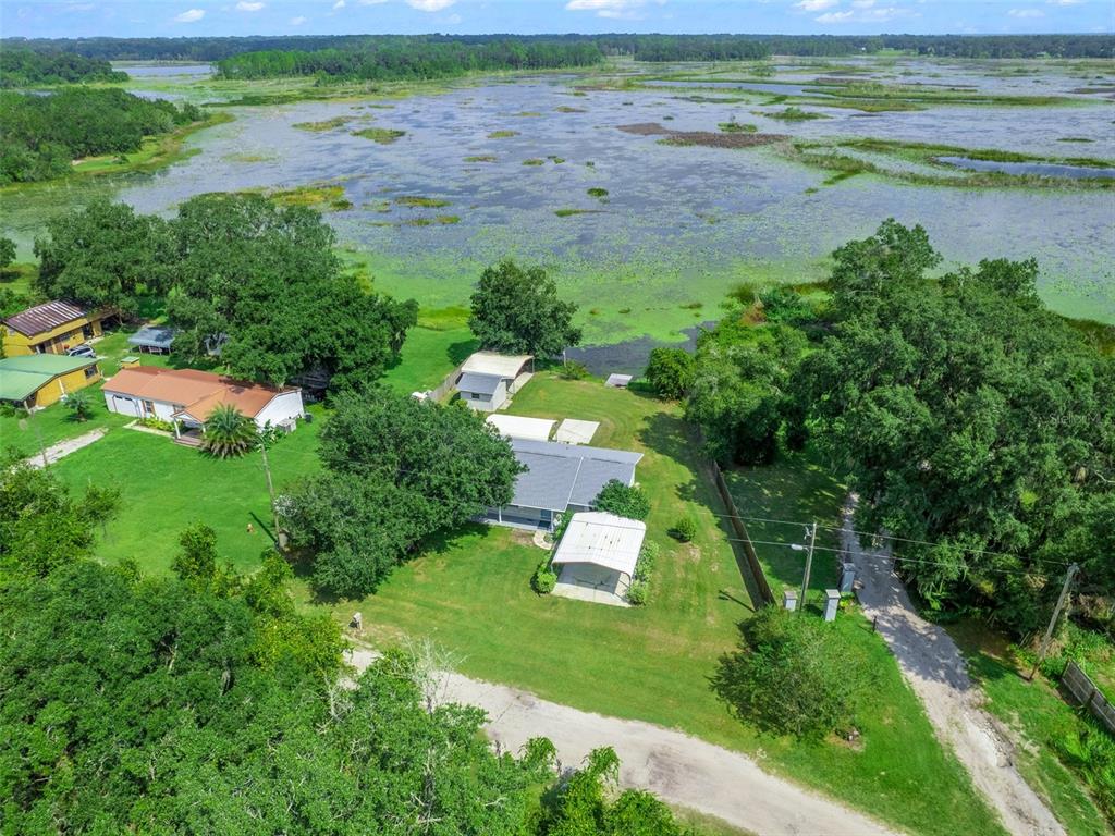 An aerial view shows a house with a carport and outbuildings near a large lake — 11495 SE 121ST LANE ROAD, BELLEVIEW, FL