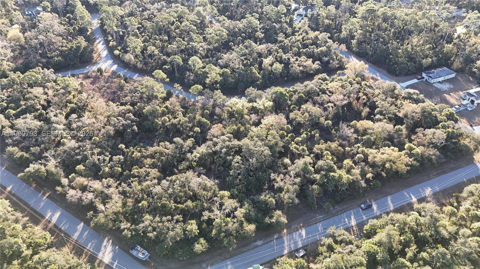An aerial view shows a wooded lot bordered by paved roads and nearby houses — 0 BACKERT RD, North Port FL 34291, NORTH PORT, FL