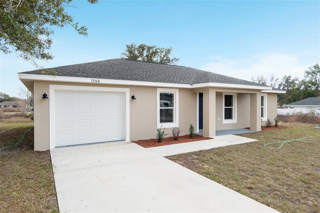 A single-story house with a beige stucco exterior, a one-car garage, and a covered porch — 15393 SW 26TH PLACE, OCALA, FL