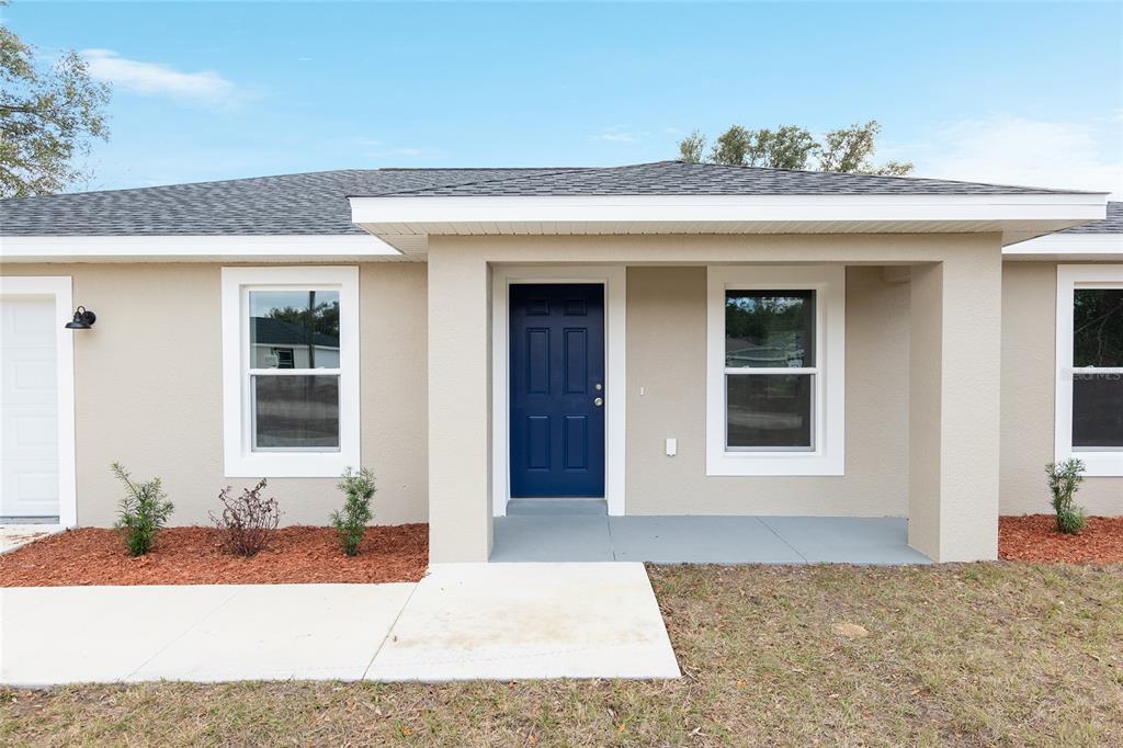 A single-story house exterior features a blue front door, a covered porch, and tan siding — 15393 SW 26TH PLACE, OCALA, FL