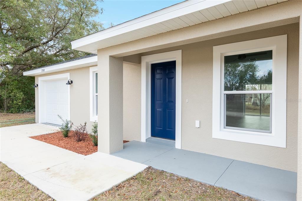 A tan house exterior features a blue front door, a white garage, and a concrete porch — 15393 SW 26TH PLACE, OCALA, FL