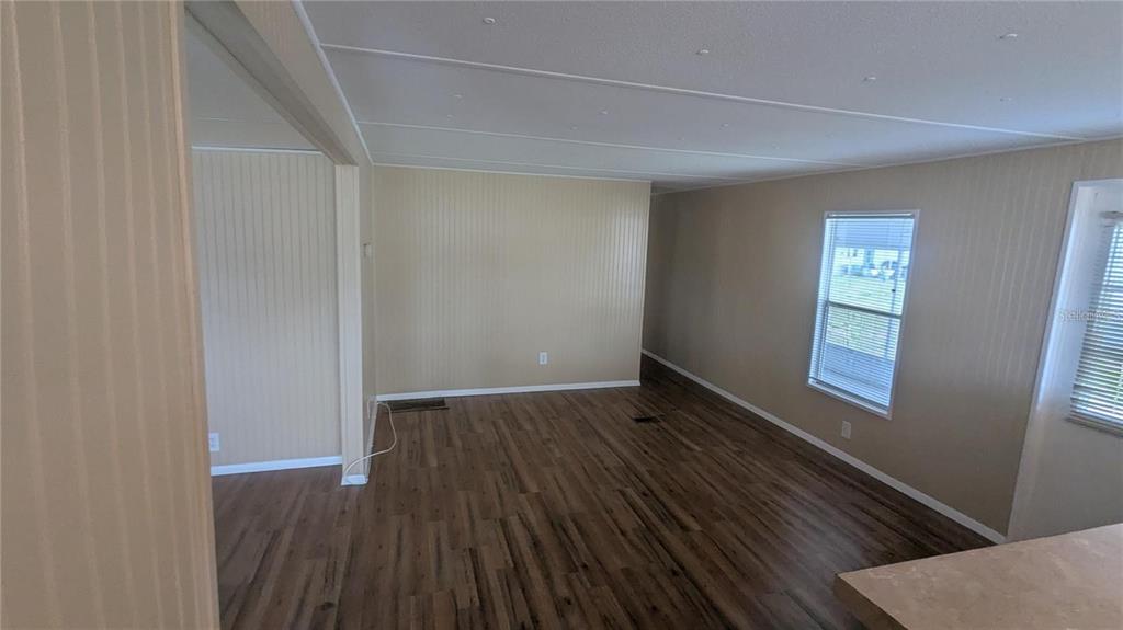 An empty living room features light-colored paneled walls, wood-look flooring, and two windows — 39518 STERLING DRIVE, ZEPHYRHILLS, FL