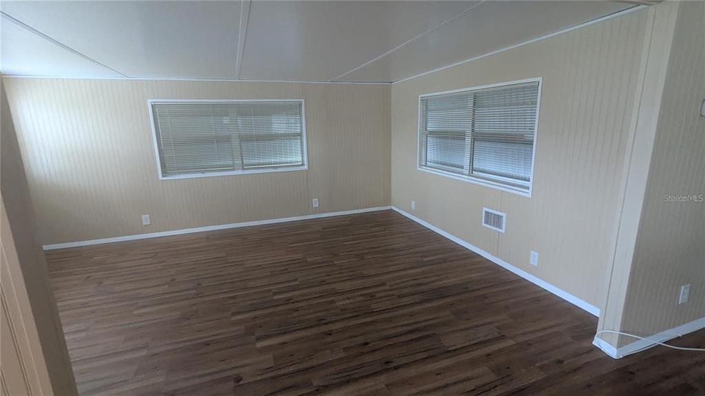 An empty room features light-colored paneled walls, wood-look flooring, and two windows with blinds — 39518 STERLING DRIVE, ZEPHYRHILLS, FL