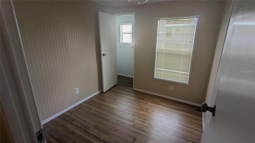 A bedroom with wood-look flooring, vertical paneling on one wall, and a window with blinds — 39518 STERLING DRIVE, ZEPHYRHILLS, FL