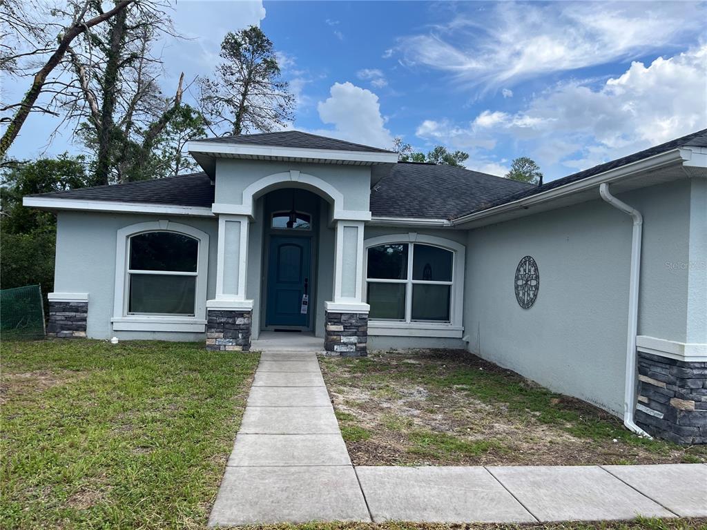 A light blue house with a stone-accented entryway and a concrete walkway — 2404 LEMA DRIVE, SPRING HILL, FL