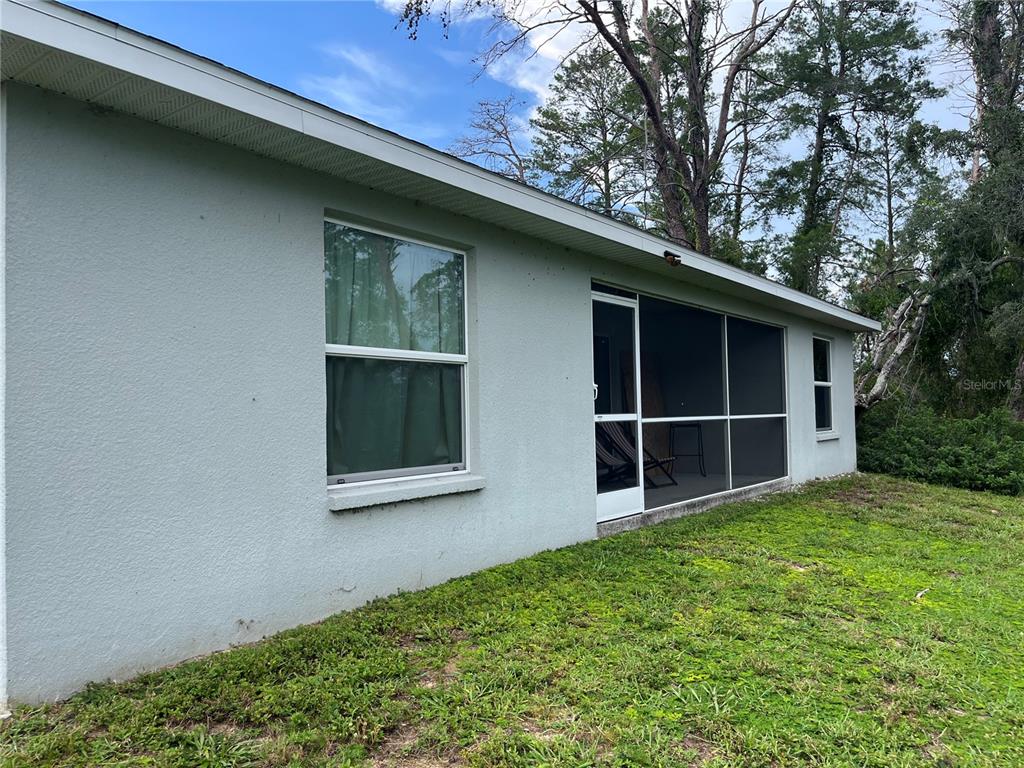 The exterior of a house features a light-colored stucco wall, a window, and a screened-in porch — 2404 LEMA DRIVE, SPRING HILL, FL