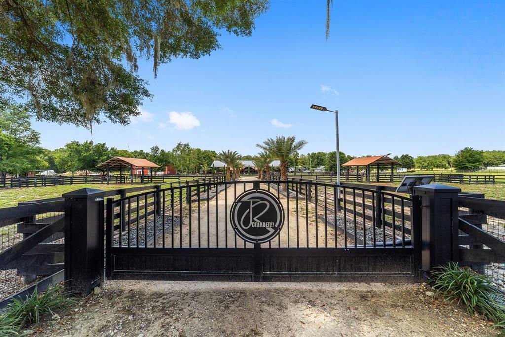 A black metal gate with a circular logo opens to a fenced equestrian property — 16392 NE JACKSONVILLE ROAD, CITRA, FL