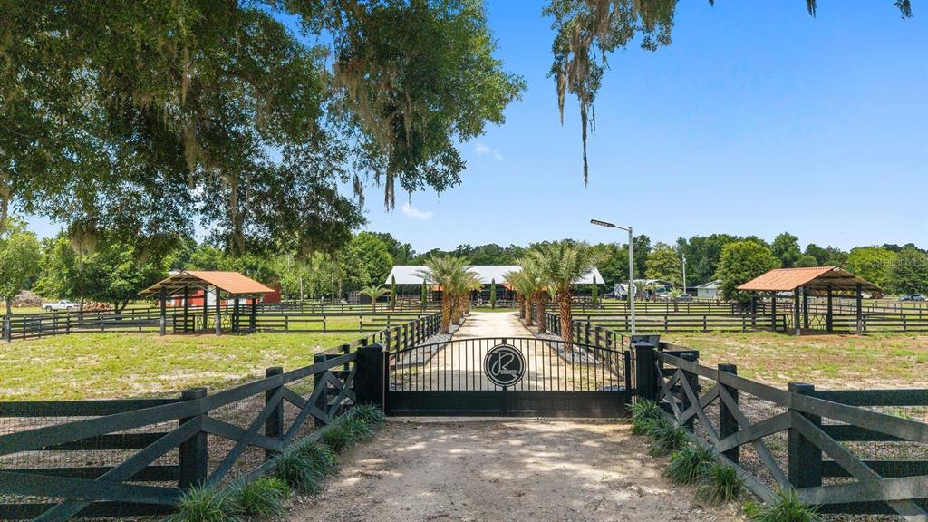 A gated entrance leads to a gravel driveway flanked by fenced pastures and palm trees — 16392 NE JACKSONVILLE ROAD, CITRA, FL