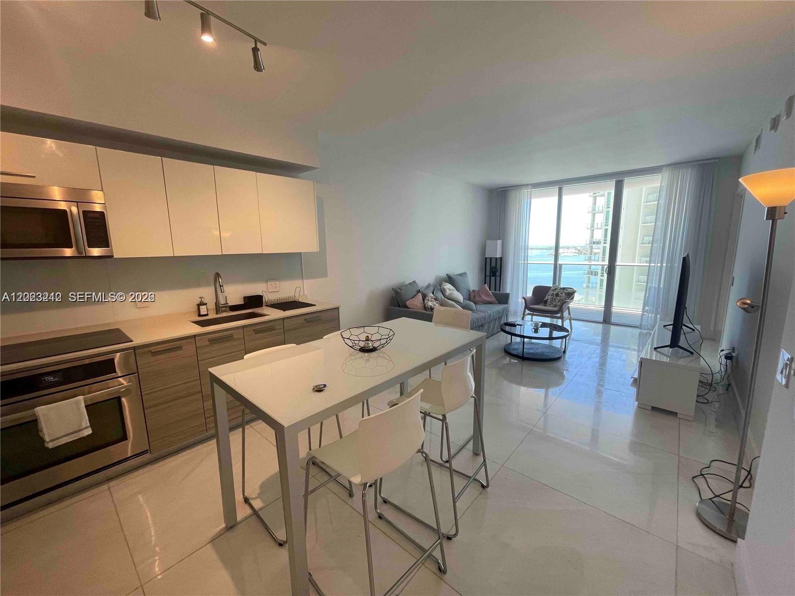 A modern open-concept kitchen and living area features white cabinetry, tile floors, and balcony views — 1300 Brickell Bay Dr # 2304, Miami FL 33131, MIAMI, FL