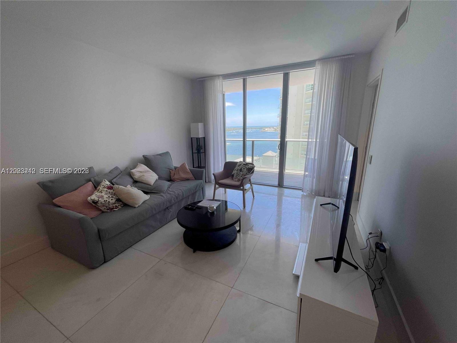 A living room features a gray sofa, a round coffee table, and a balcony view — 1300 Brickell Bay Dr # 2304, Miami FL 33131, MIAMI, FL