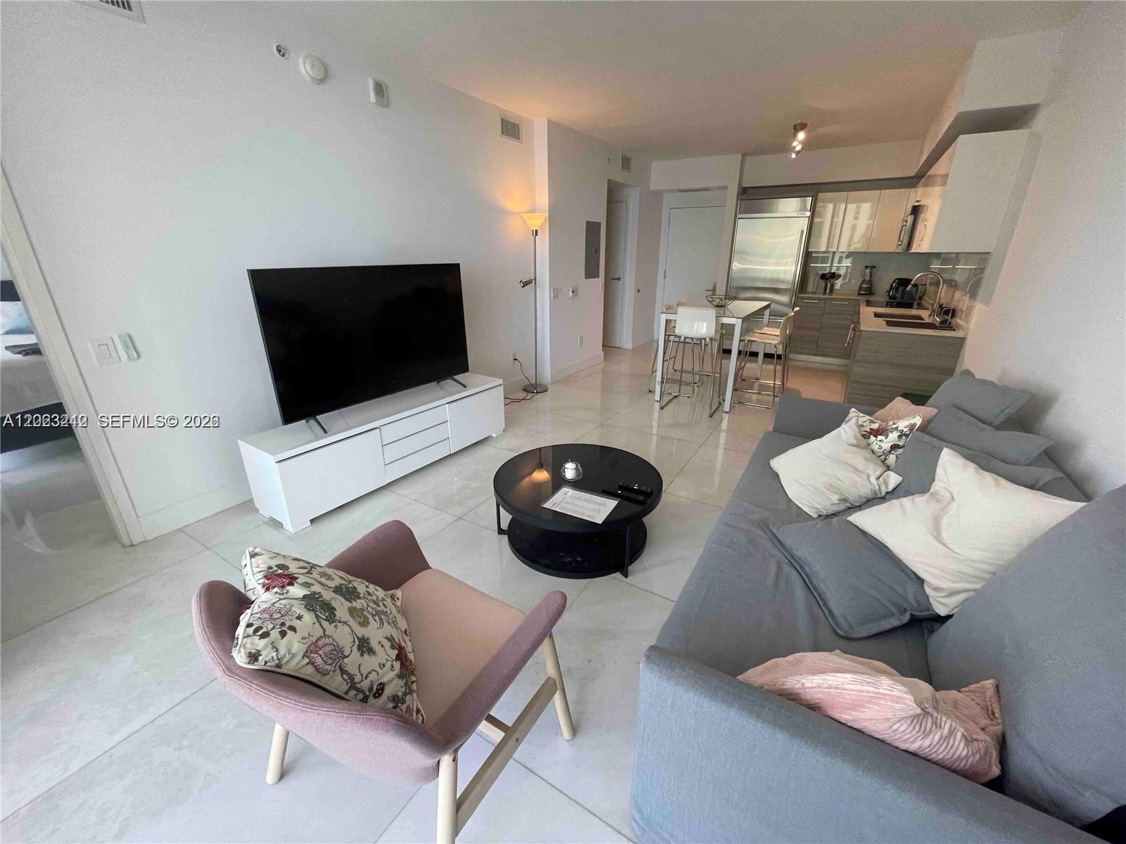 A modern living room features a grey sofa, a pink armchair, and an open kitchen — 1300 Brickell Bay Dr # 2304, Miami FL 33131, MIAMI, FL