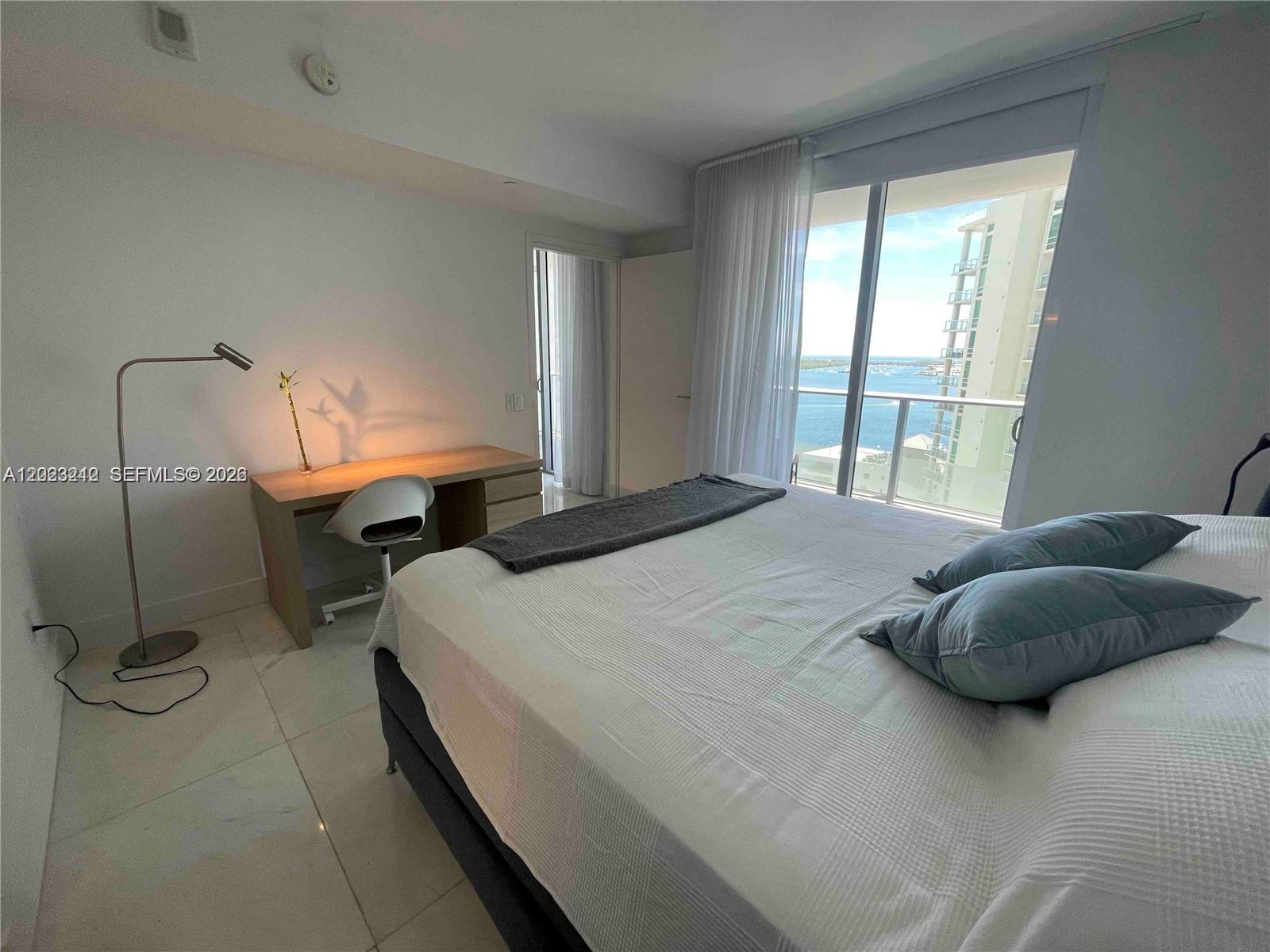 A bedroom features a bed, a desk with a lamp, and a balcony overlooking water — 1300 Brickell Bay Dr # 2304, Miami FL 33131, MIAMI, FL