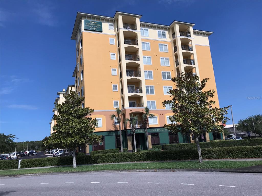 A multi-story yellow hotel building features balconies and a ground-level pub under a blue sky — 8112 POINCIANA BOULEVARD UNIT 1302, ORLANDO, FL