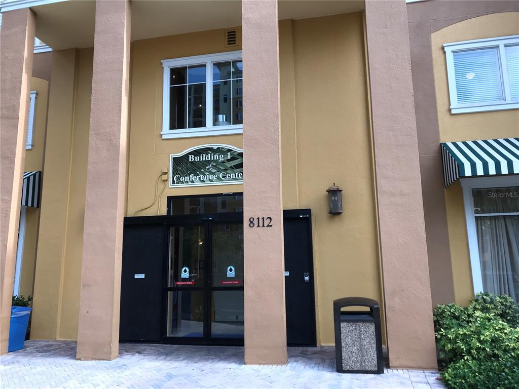 The exterior entrance of a building features a sign, glass doors, and a trash receptacle — 8112 POINCIANA BOULEVARD UNIT 1302, ORLANDO, FL