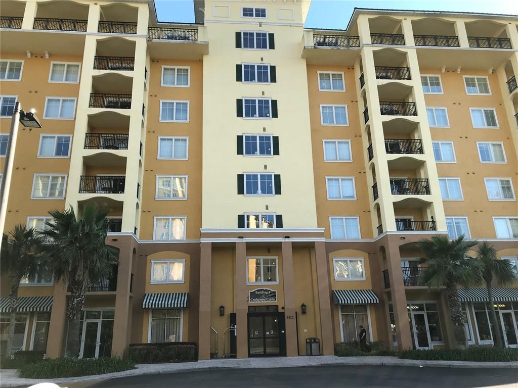 A multi-story yellow apartment building features a central entrance, balconies, and palm trees in front — 8112 POINCIANA BOULEVARD UNIT 1302, ORLANDO, FL