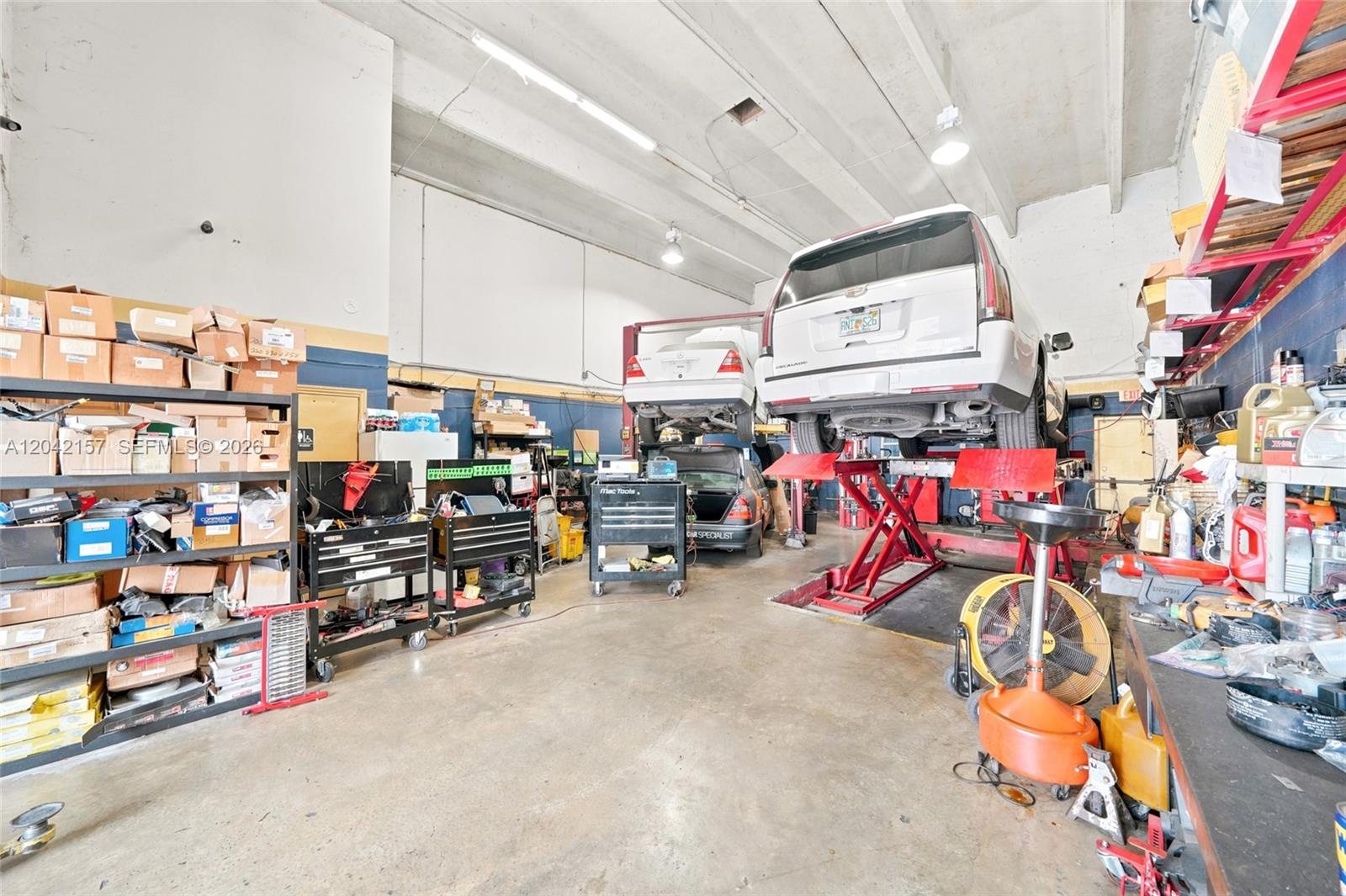 This auto repair shop features a vehicle lift, storage shelving, and various automotive tools — 11951 SW 144th Ct, Miami FL 33186, MIAMI, FL