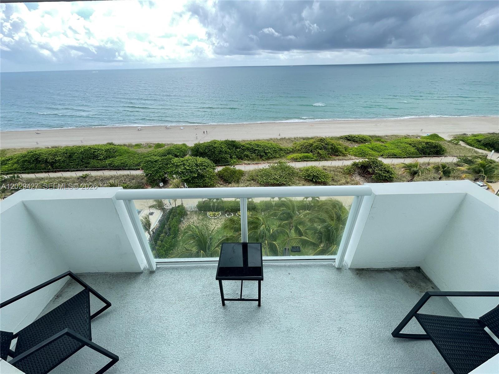 A balcony with two black chairs and a small table overlooks the beach and ocean — 9195 Collins Ave # 1001, Surfside FL 33154, SURFSIDE, FL