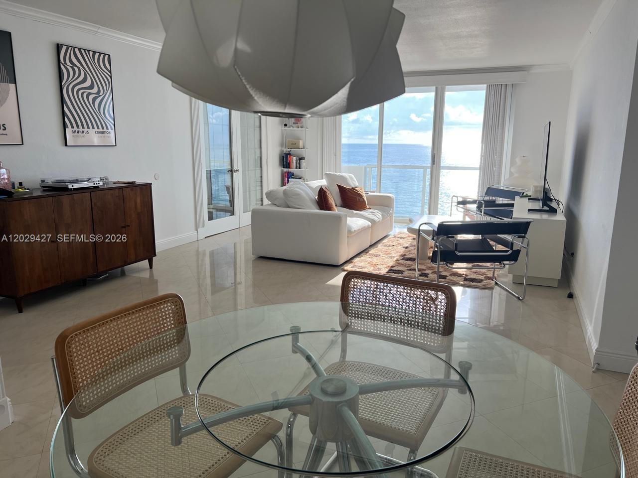 A dining area with a glass table overlooks a living room with ocean views — 9195 Collins Ave # 1001, Surfside FL 33154, SURFSIDE, FL