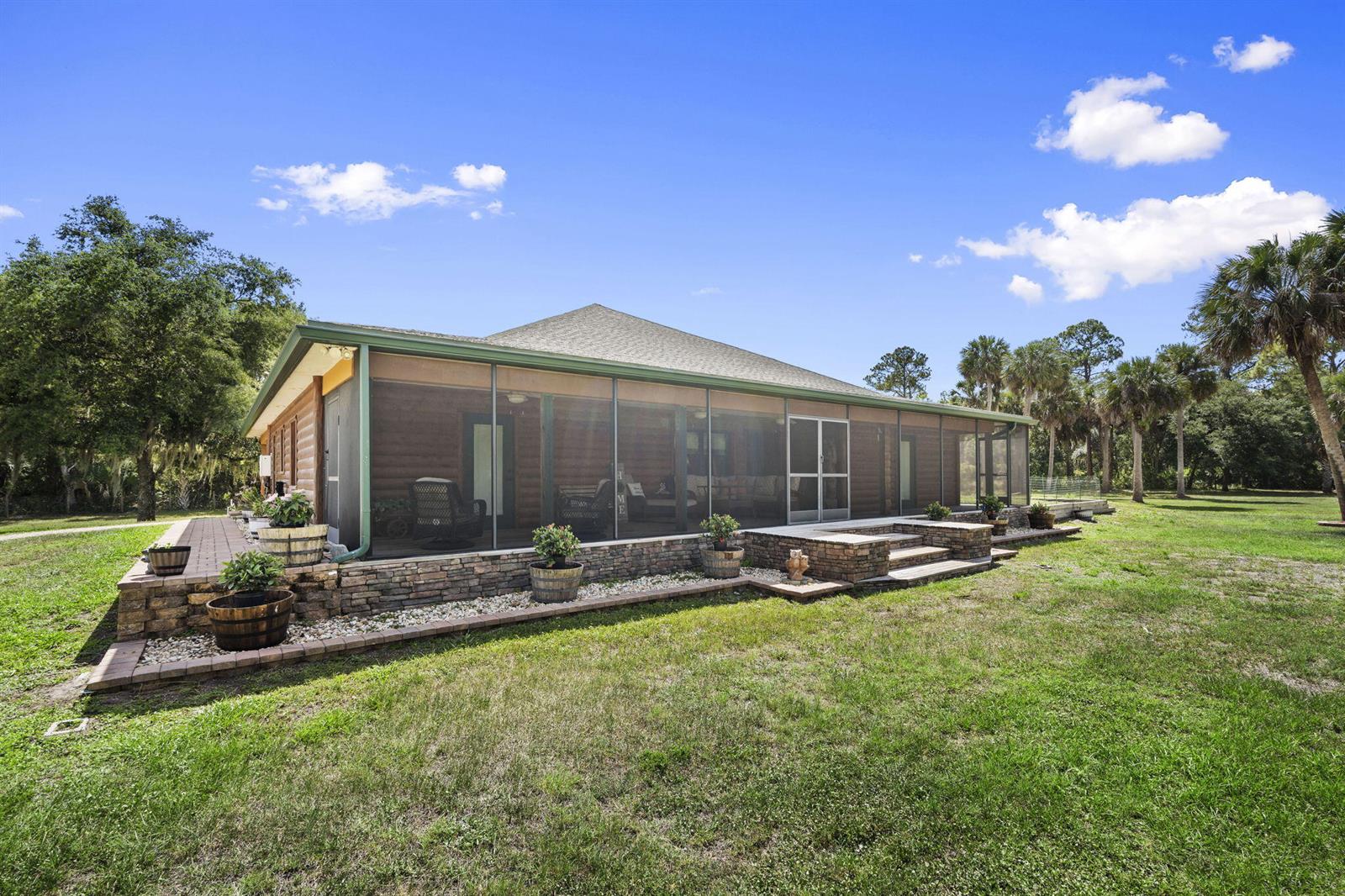 A log cabin home features a large screened-in porch and a stone-walled patio area — 32801 N Us Highway 441 N # 52, Okeechobee FL 34972, OKEECHOBEE, FL