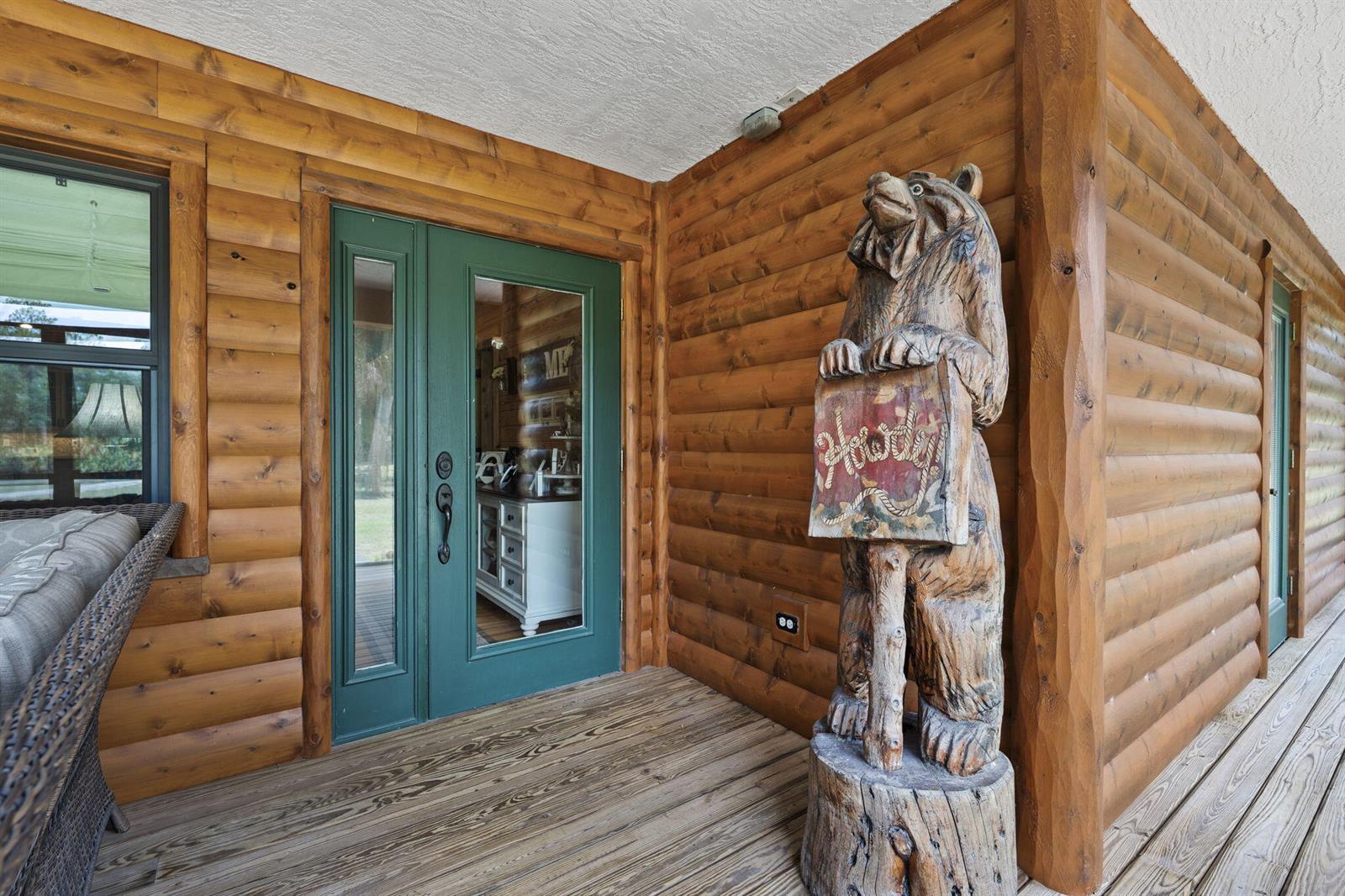 A wooden porch features a carved bear statue holding a sign next to a green door — 32801 N Us Highway 441 N # 52, Okeechobee FL 34972, OKEECHOBEE, FL