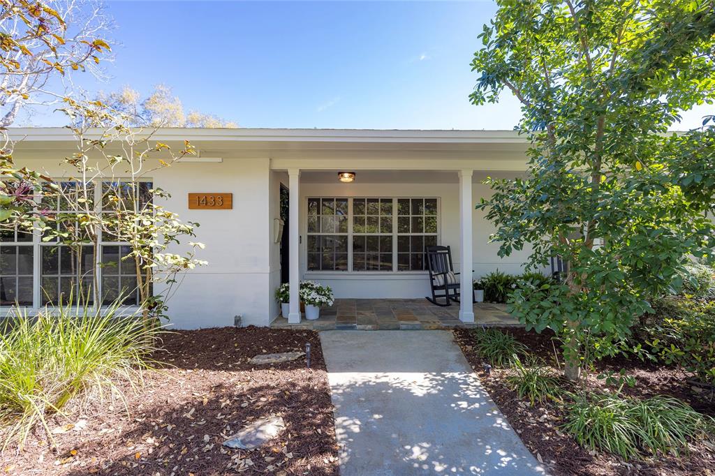 A white single-story house exterior features a covered porch, stone flooring, and a concrete walkway — 1433 PARK STREET N, ST PETERSBURG, FL