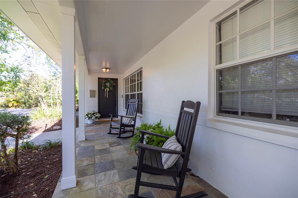 A covered front porch features slate tile flooring, two black rocking chairs, and a front door — 1433 PARK STREET N, ST PETERSBURG, FL