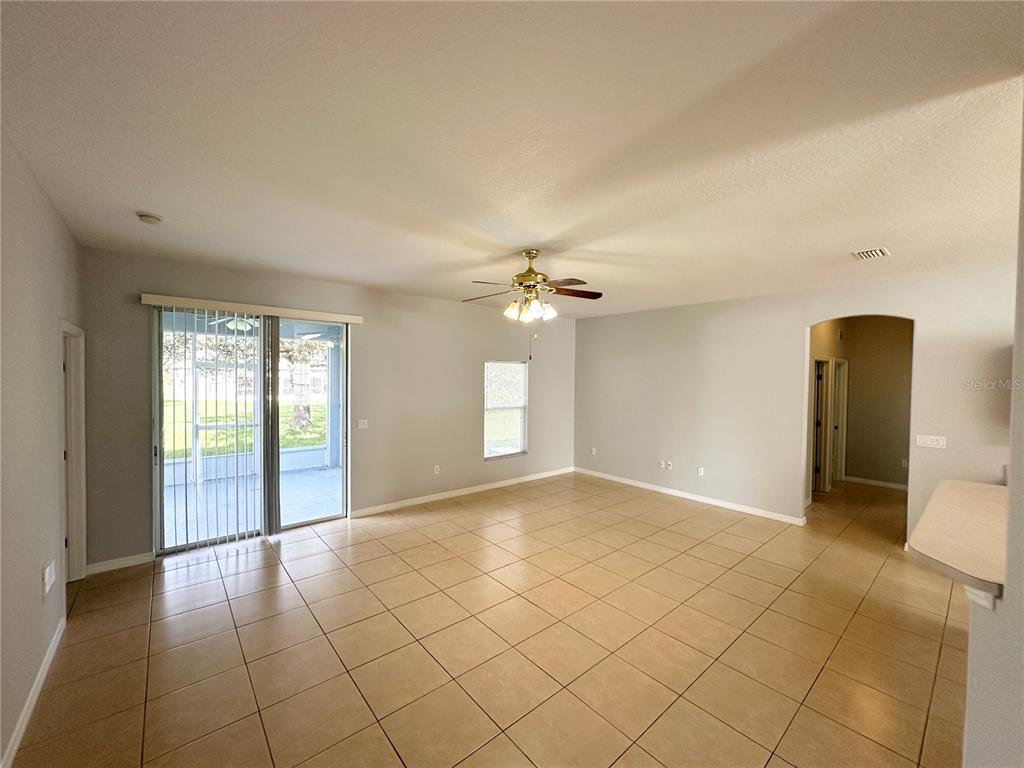 An empty living room features light-colored tile flooring, a ceiling fan, and sliding glass doors — 11 PRAVER LANE, PALM COAST, FL
