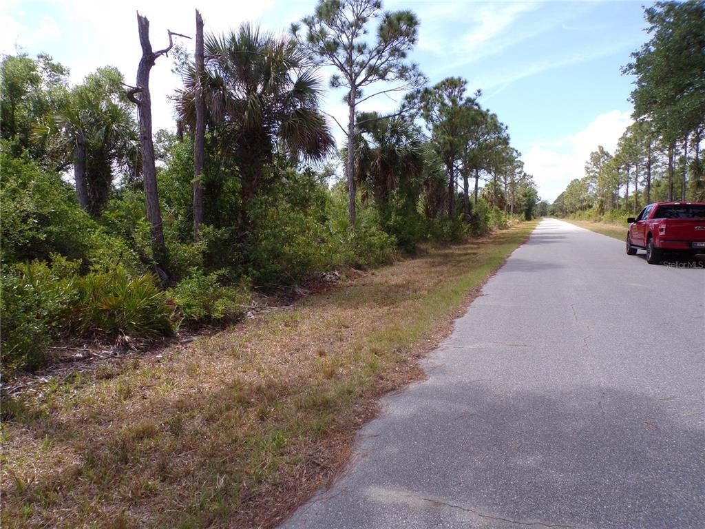 A red pickup truck is parked on the side of a paved road near wooded land — 2300 REMAGEN STREET, PORT CHARLOTTE, FL