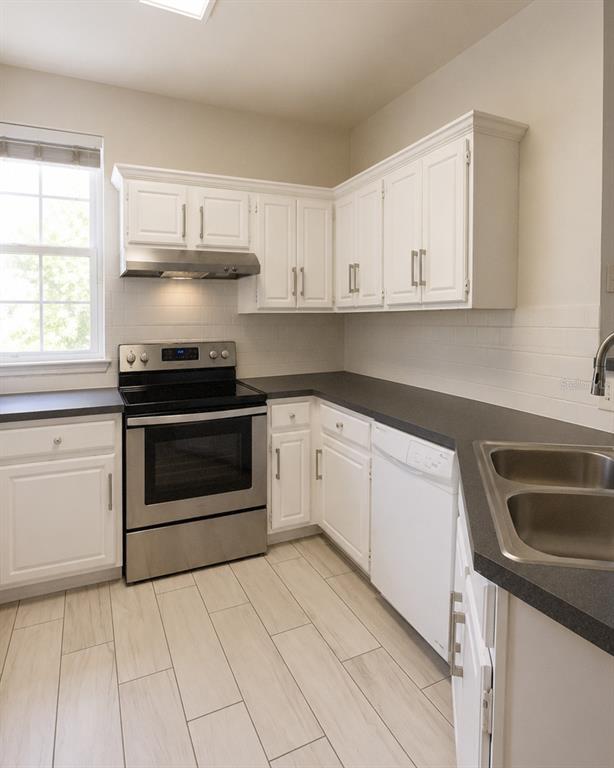 A kitchen features white cabinets, stainless steel appliances, dark countertops, and light-colored tile flooring — 3213 GREENWICH VILLAGE BOULEVARD UNIT 102, ORLANDO, FL
