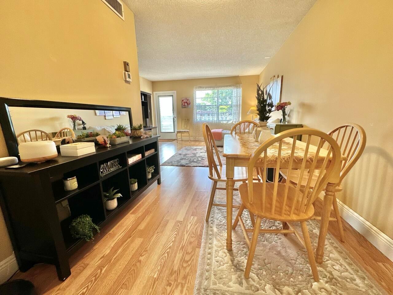 A dining area with a wooden table and chairs sits beside a black shelving unit — 19 Abbey Lane # 204, Delray Beach FL 33446, DELRAY BEACH, FL