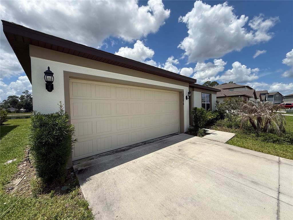 A beige garage door is attached to a house with white stucco and brown trim — 30596 THUNDERBIRD DRIVE, WESLEY CHAPEL, FL