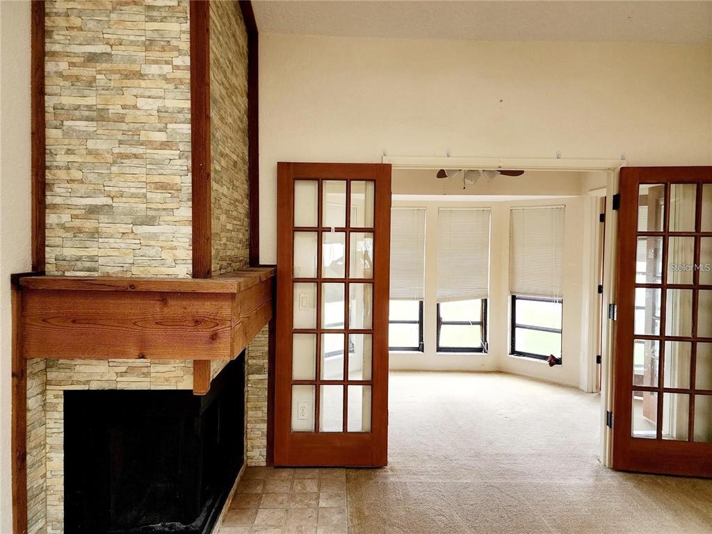A stone fireplace with a wooden mantel sits beside French doors leading to a sunroom — 4356 MIDDLEBROOK ROAD UNIT 3, ORLANDO, FL