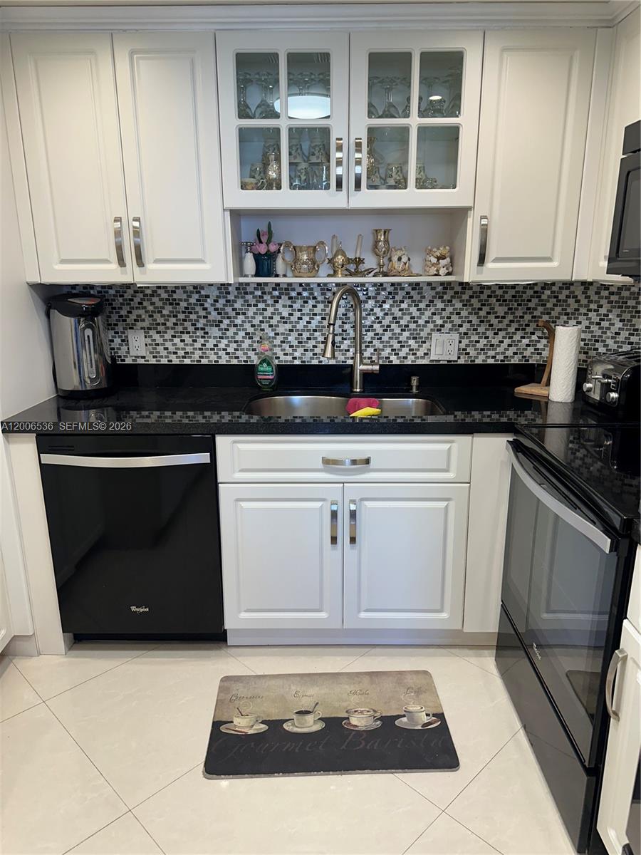 A kitchen features white cabinets, black countertops, a mosaic backsplash, and black appliances — 1985 S Ocean Dr # 21P, Hallandale Beach FL 33009, HALLANDALE BEACH, FL
